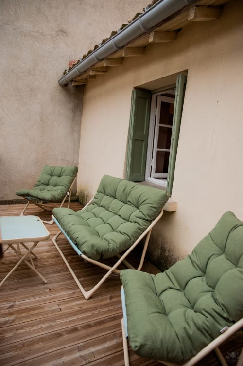 Chaises longues vertes rembourrées sur la terrasse en bois de la maison d'hôtes La Maison de Marcelo à Carcassonne avec bâtiment en pierre
