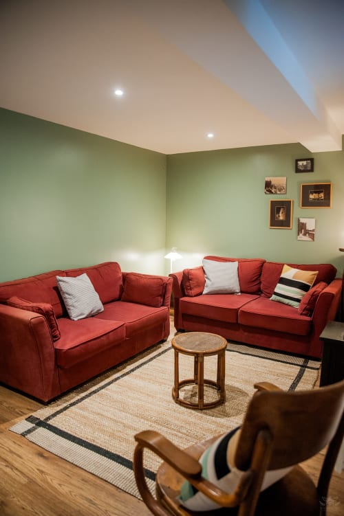 Salon moderne avec canapés rouges, murs verts et mobilier en bois dans un gîte de Carcassonne
