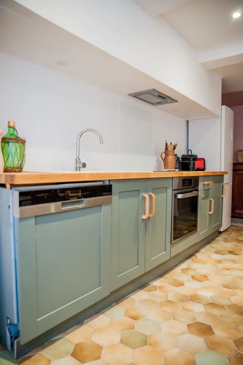 Cuisine moderne avec armoires vert sauge, plan de travail en bois et carrelage en terre cuite au gîte La Maison de Marcelo