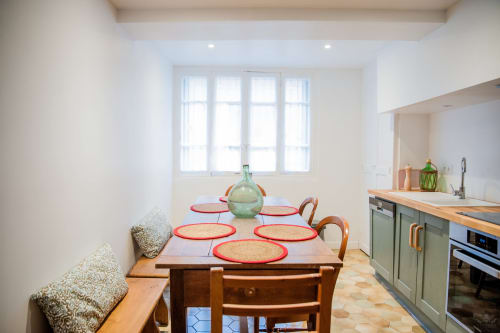 Cuisine-salle à manger lumineuse du cottage Mi Casa Es Su Casa à Carcassonne, avec table en bois, sets de table rouges et appareils modernes.