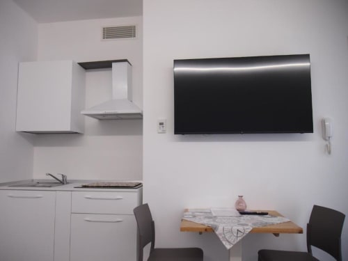 Suite junior moderna dell'Hotel Vienna a Pesaro: angolo cottura con TV a parete, mobili bianchi e tavolo da pranzo
