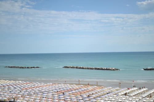 Spiaggia di Pesaro con ombrelloni colorati e lettini, Mare Adriatico turchese e frangiflutti sotto cielo blu