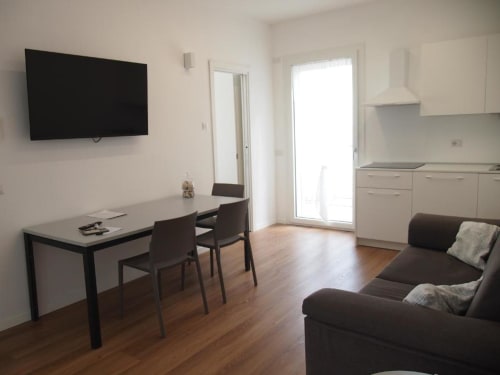 Suite Junior Hotel Vienna a Pesaro con zona pranzo moderna, TV schermo piatto, cucina bianca e divano marrone su pavimenti in legno