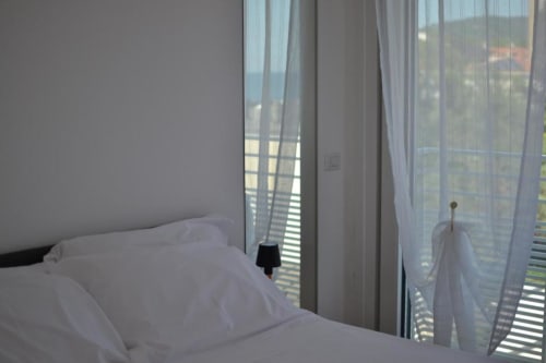 Junior Suite luminosa all'Hotel Vienna Pesaro con biancheria bianca, tende trasparenti, accesso al balcone e vista laterale sul mare