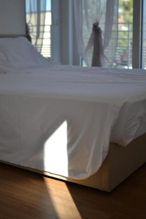 Letto biancheria bianca nella junior suite dell'Hotel Vienna Pesaro con vista mare, luce solare che filtra dalle finestre con tende trasparenti