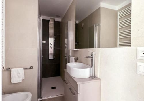 Bagno moderno della junior suite Hotel Vienna con lavabo tondo bianco, grande specchio, doccia, porta asciugamani e piastrelle in marmo