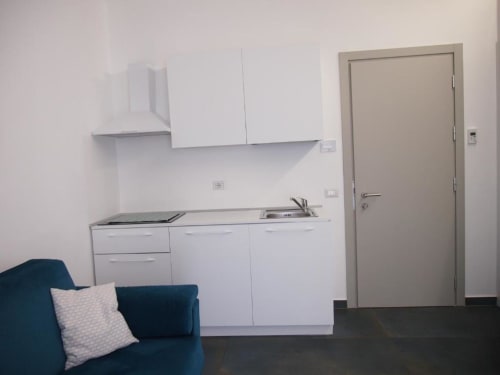 Piccola cucina moderna con mobili bianchi, pavimento scuro, sedute blu, e porta della suite junior Hotel Vienna Pesaro