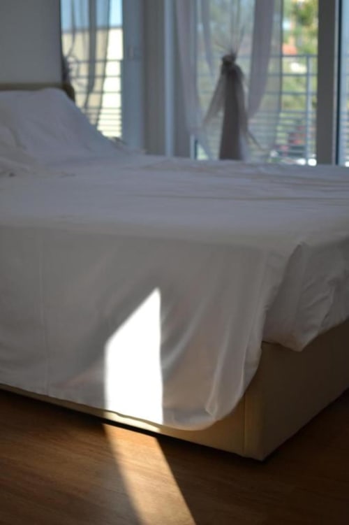 Sonnendurchflutete Superior Suite im Hotel Vienna in Pesaro mit weißer Bettwäsche, Holzboden und Balkon mit Blick auf Stadt und Meer
