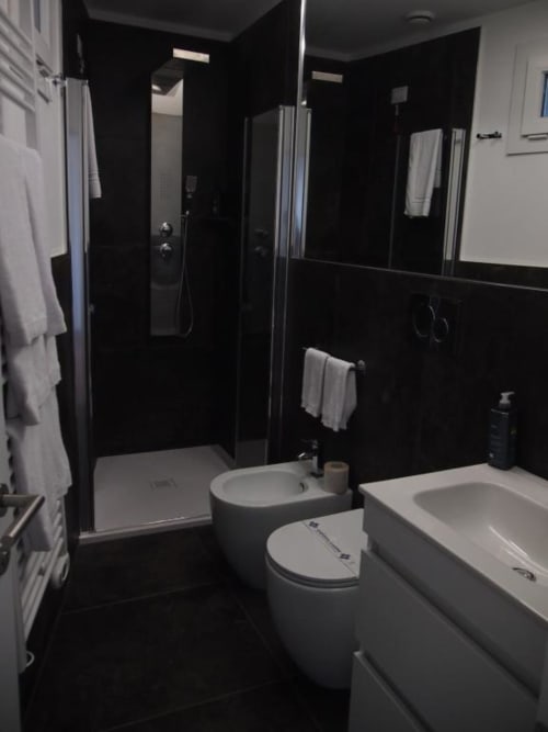 Modernes Badezimmer in der Hotel Vienna Superior Suite mit schwarzen Wänden, weißen Armaturen, gläserner Duschkabine und Marmorboden