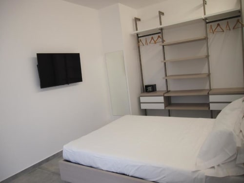 Camera moderna dell'Hotel Vienna Pesaro con letto bianco, TV a parete, armadio con specchi e scaffali con appendiabiti