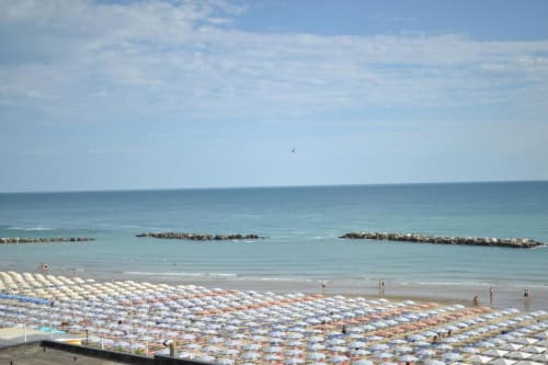Spiaggia di Pesaro con ombrelloni e lettini colorati, mare turchese calmo, frangiflutti e bagnanti