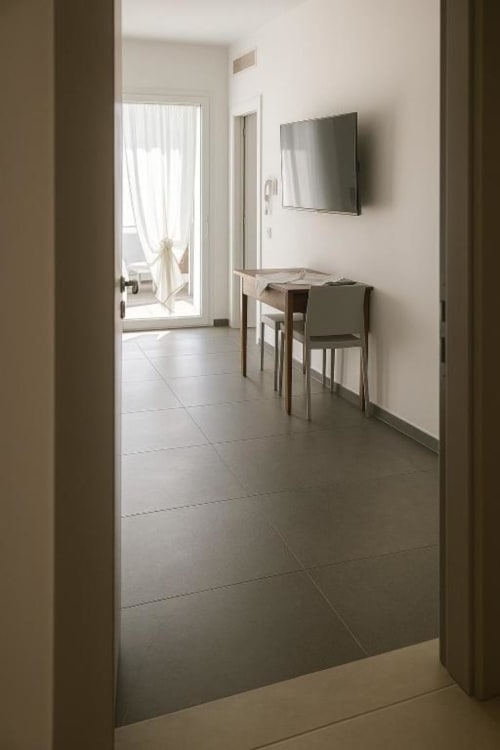 Camera moderna dell'Hotel Vienna a Pesaro con pavimento in piastrelle, TV a parete, tavolo da pranzo e porta in vetro che conduce a