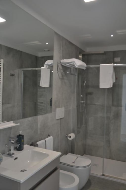 Bagno moderno della Suite Superiore Hotel Vienna a Pesaro, con doccia in piastrelle grigie, lavabo bianco, wc e portasciugamani