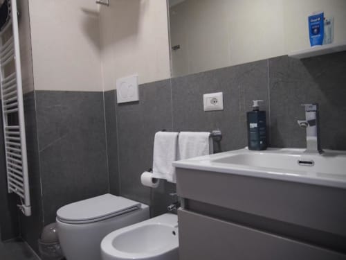 Bagno moderno della Suite Superior Hotel Vienna a Pesaro con pareti in piastrelle scure, lavabo bianco, bidet e servizi inclusi