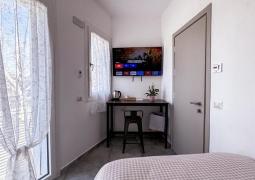 Camera singola ampia Hotel Vienna Pesaro con scrivania, TV schermo piatto, sedia nera, biancheria rosa e vista città dalla finestra