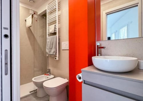 Bagno dell'Hotel Vienna a Pesaro con lavabo bianco, wc, bidet e caratteristica parete rossa con area doccia