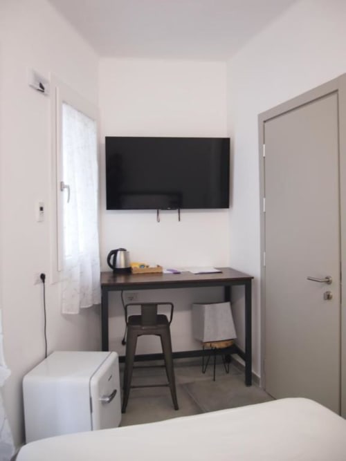 Camera moderna dell'Hotel Vienna di Pesaro con scrivania, TV a parete, sedia nera, bollitore e letto bianco