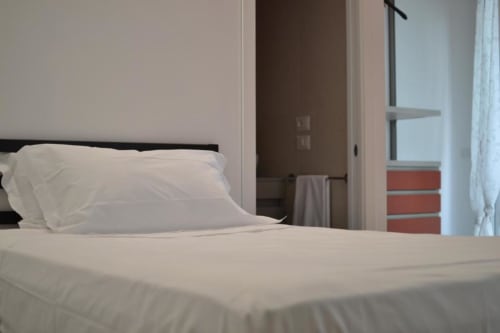 Camera moderna dell'Hotel Vienna a Pesaro con biancheria bianca, testata scura, bagno en-suite aperto e vista sulla città