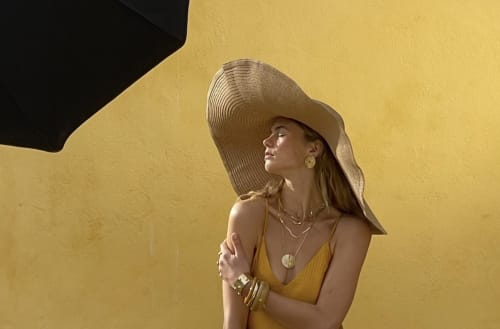 Woman in yellow dress and wide-brimmed hat against yellow wall at Le Domaine du Fortin, Ménerbes