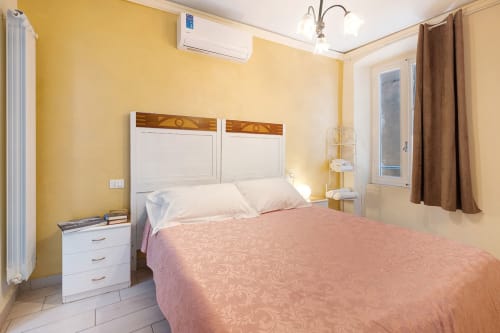 Camera da letto gialla luminosa con letto matrimoniale, comodino bianco e finestra presso Casa Scola Loano B&B in Italia