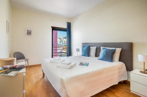 Quarto luminoso na Villa Odyssey em Albufeira com cama de casal, detalhes em azul e varanda com vista para a cidade
