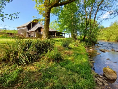 Rustic cottage by stream at Le gite des mousquetaires, Lanne en Baretous, surrounded by green trees and meadow