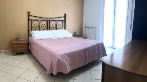 Spaziosa camera da letto a Casa Scola Loano con letto in ferro battuto, copriletto rosa e porte-finestre sulla terrazza a Loano, Italia