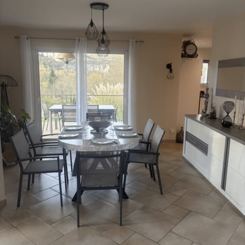 Salle à manger moderne avec table ronde, chaises noires, luminaires suspendus et vue sur un paysage forestier à la Villa des
