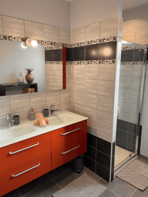 Salle de bain moderne avec vasque rouge, carrelage beige et douche vitrée au Gîte la Villa des Falaises du Lot