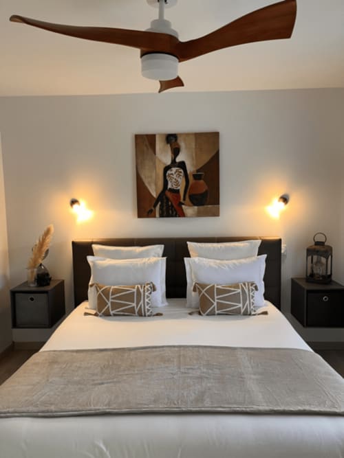 Chambre moderne du Gîte la Villa des Falaises du Lot avec ventilateur de plafond, appliques murales, œuvres d'art et coussins géométriques
