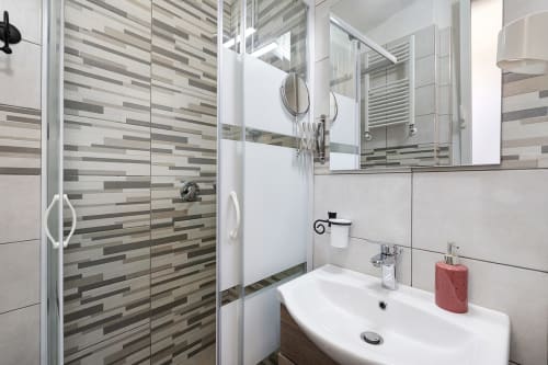 Modern bathroom at Casa Scola Loano B&B in Loano, Italy with striped tile shower, white sink, and mirror