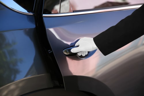 Persona in abbigliamento formale che apre la portiera di un'auto di lusso presso l'hotel Le Arche di Verona