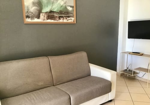 Comfortable lounge area at Casa Scola Loano with beige sofa, green accent wall, and wall-mounted TV