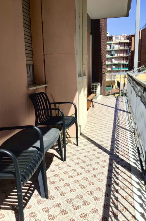Sunny balcony with black chairs at Casa Scola Loano, overlooking residential buildings in Loano, Italy