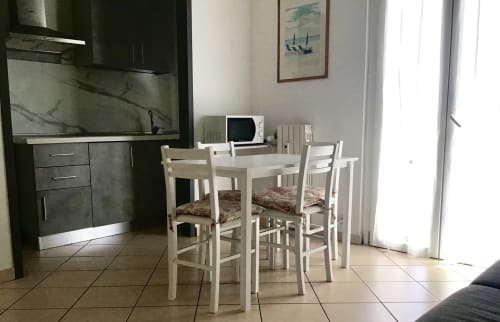 Casa Scola Loano dining area with white table, chairs, and kitchenette overlooking balcony
