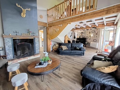 Open-plan living area at Le gite des mousquetaires with fireplace, wooden stairs, blue accent wall, and black leather seating