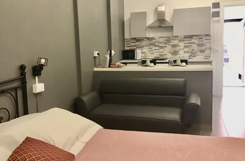 Modern studio bedroom at Casa Scola Loano with gray sofa, bed with coral bedding, and kitchenette in Loano, Italy