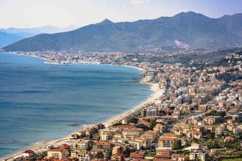 Litorale di Loano con spiaggia dorata, acque turchesi del Mediterraneo e edifici colorati incastonati tra le montagne, Italia
