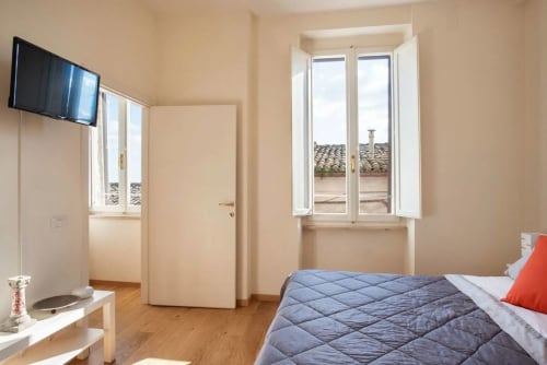 Camera luminosa dell'Appartamento Proprietà Clara ad Assisi, con letto trapuntato blu, TV, pavimenti in legno e finestre con vista