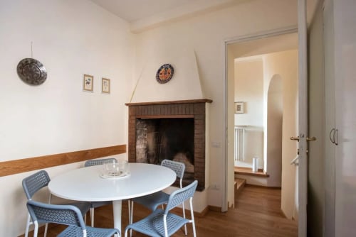 Zona pranzo dell'appartamento Casa Clara ad Assisi, con tavolo rotondo, sedie blu, camino e porta verso la stanza adiacente