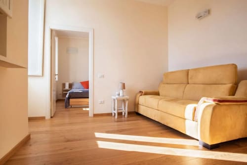 Luminoso soggiorno con divano in pelle gialla presso l'appartamento Casa Clara ad Assisi, pavimenti in legno e accesso alla camera da letto