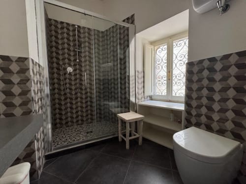 Bagno moderno con piastrelle geometriche, box doccia in vetro, vasca bianca freestanding e finestra a Casa Clara ad Assisi