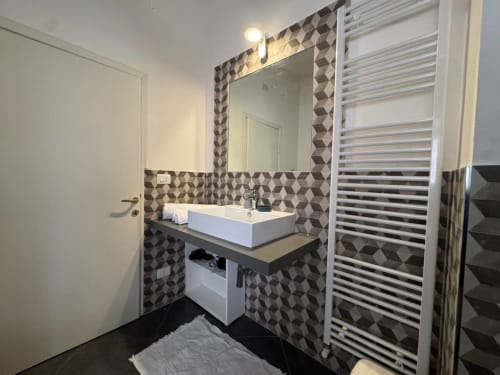 Bagno moderno a Casa Clara ad Assisi con pareti piastrellate geometriche, lavabo da appoggio, scaldasalviette e specchio illuminato