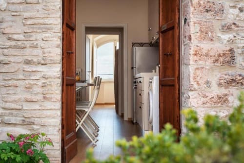 Porte in legno che si aprono sulla luminosa cucina dell'hotel ad Assisi con elettrodomestici e muri in pietra visibili