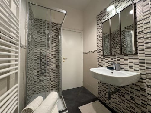 Bagno moderno a Casa Clara Dependance ad Assisi con rivestimento in mosaico, doccia a filo pavimento, lavabo bianco e scaldasalviette