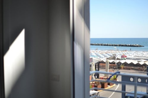 Vista dal balcone dell'Hotel Vienna a Pesaro: spiaggia con ombrelloni, passeggiata lungomare e mare Adriatico