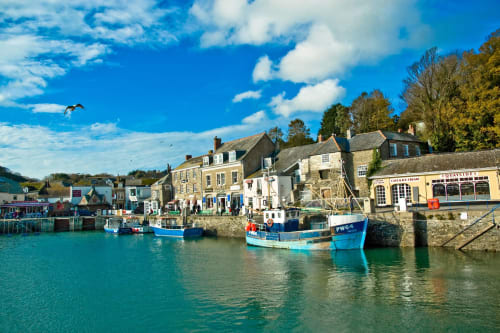 Picturesque Padstow harbor with blue fishing boats, historic stone buildings, and waterfront shops on a sunny day