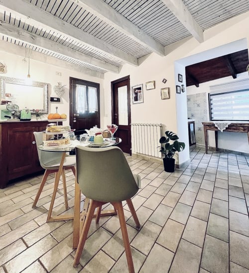 Salle à manger moderne dans l'appartement Agritusmo Stecadò avec table ronde, chaises vertes, plafond aux poutres apparentes et accès à la cuisine