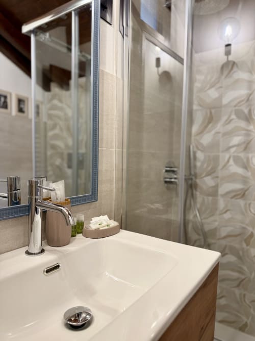 Salle de bain moderne de l'appartement Agritusmo Stecadò avec lavabo blanc, robinetterie chromée, miroir et douche ouverte à carrelage motifs