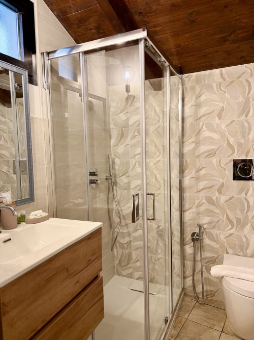 Salle de bain moderne avec douche vitrée, carrelage beige à motifs, meuble-lavabo en bois et toilettes à Agritusmo Stecadò